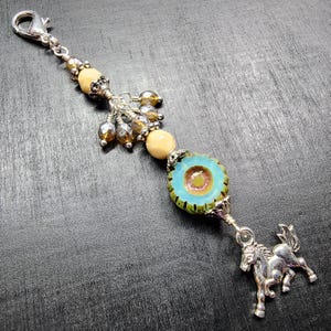 Puede incluir: Un dije de metal plateado con cierre de langosta, una serie de cuentas de color canela claro y ámbar translúcido, una cuenta de vidrio redonda de color turquesa con borde festoneado y un colgante de caballo de metal plateado en la base.