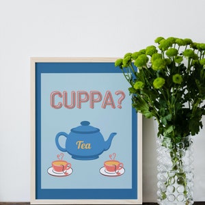 Könnte beinhalten: Ein gerahmter Druck mit blauem Hintergrund und dem Text "CUPPA?" in Rosa. Eine blaue Teekanne mit dem Wort "Tea" in Gelb befindet sich in der Mitte des Drucks. Zwei rote Teetassen mit Dampf befinden sich auf beiden Seiten der Teekanne.