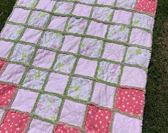 Puede incluir: Una colcha de retazos rosa y verde con una variedad de patrones, incluyendo estrellas, animales y cuadros. La colcha está hecha de una tela suave y esponjosa y tiene un borde rizado.