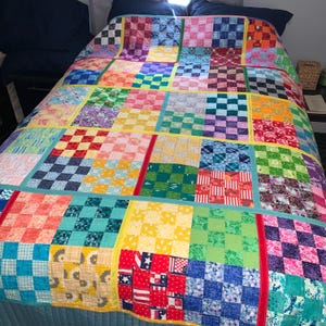 May include: A patchwork quilt featuring a grid of multicolored fabric squares in various patterns, including floral, geometric, and star motifs. The squares are separated by solid-colored fabric sashing in yellow, red, and teal.
