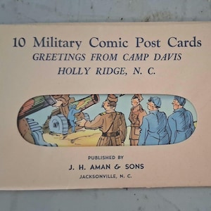 May include: A vintage postcard set titled "10 Military Comic Post Cards" with a cutout revealing a cartoon scene of soldiers and a cannon. The card is tan with text that reads "Greetings from Camp Davis, Holly Ridge, N.C." and "Published by J.H. Aman & Sons, Jacksonville, N.C."