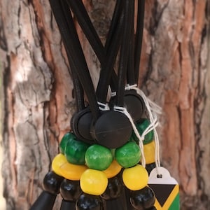 Op de afbeelding: Een set zwarte elastische koordarmbanden met groene, gele en zwarte kralen. Elke armband heeft een klein label met de Jamaicaanse vlag.