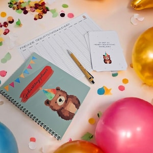 Op de afbeelding: Een verjaardagsthema met een spiraalgebonden planner, een pen en een stapel kaarten. De planner heeft een berenillustratie en de tekst "Geburtstagsplaner". Kleurrijke ballonnen en confetti omringen de items, wat een feestelijke sfeer creëert.