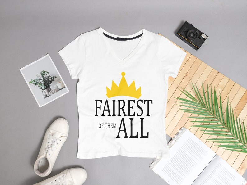 May include: White V-neck t-shirt with a gold crown graphic and the text "Fairest of them all".