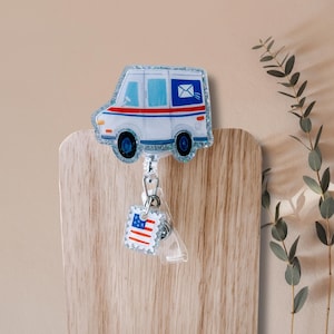 May include: A badge reel featuring a white mail truck with red and blue stripes, a blue envelope, and a glittery border. The badge reel also has a small stamp with the American flag.