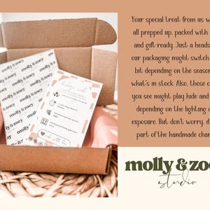Puede incluir: Una caja de cart&oacute;n marr&oacute;n abierta con dos tarjetas impresas y papel de seda rosa. Las tarjetas muestran el texto "molly & zoey" e instrucciones de cuidado. El logotipo de la marca es visible en la parte inferior de la imagen.