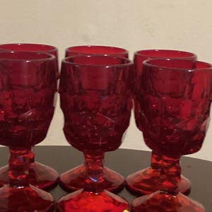 May include: Set of six red glass goblets with a textured, diamond-like pattern. The goblets have a clear, transparent base and a wide, round bowl.