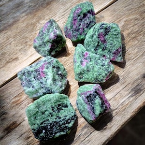 Peut inclure: Une collection de sept pierres précieuses brutes de zultanite vertes, roses et noires. Les pierres sont de forme irrégulière et de tailles variées.