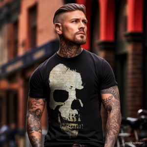 Puede incluir: Una camiseta negra con un gran gráfico de calavera blanca impreso en la parte delantera. La calavera está hecha de un documento vintage con texto. El modelo lleva la camiseta y tiene tatuajes en los brazos.