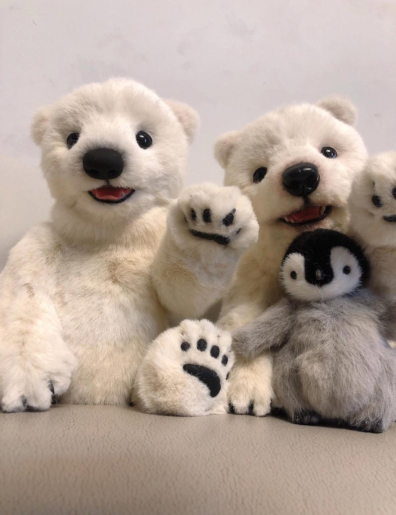 May include: Three plush toys: a white polar bear, a white polar bear cub, and a gray penguin. The polar bears are sitting up and the cub is waving. The penguin is sitting in front of the bears.