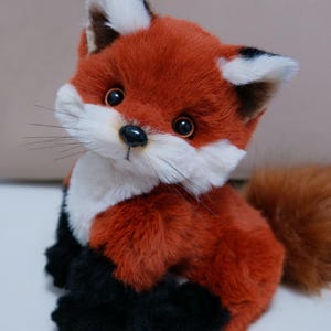 Könnte beinhalten: Ein Plüschtier in Form eines roten Fuchses mit schwarzen Pfoten und einer weißen Brust. Der Fuchs hat einen buschigen Schwanz und schwarze Augen.