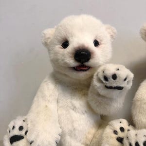 May include: A white plush polar bear teddy with black eyes, nose, and paw pads. The bear is sitting with its right paw raised in a waving gesture.