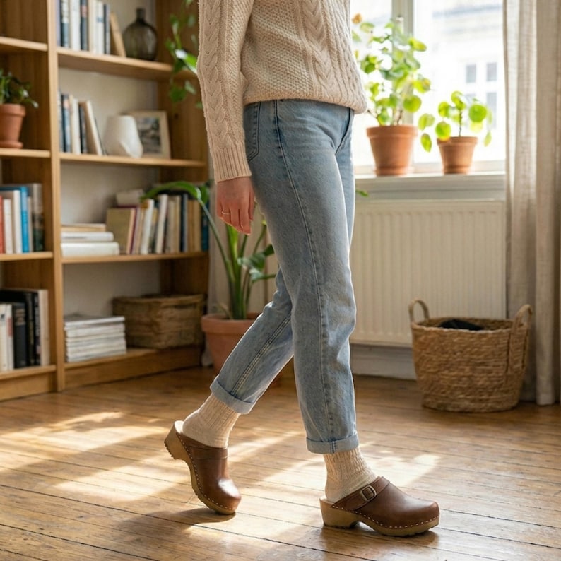 Classic Swedish wooden clogs made of natural cowhide leather in antic brown color and light wooden bottom with orthopedic profile. The upper has a strap with a buckle to adjust the length of the fastening on the heel. Available in women and men size