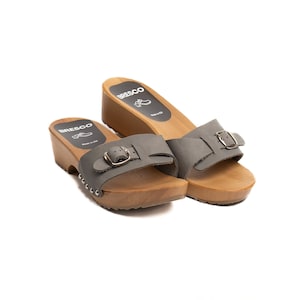 Könnte beinhalten: Ein Paar graue Ledersandalen mit Holzsohle und Schnallenriemen. Die Sandalen sind von der Marke "BRESCO" und werden in der EU hergestellt.