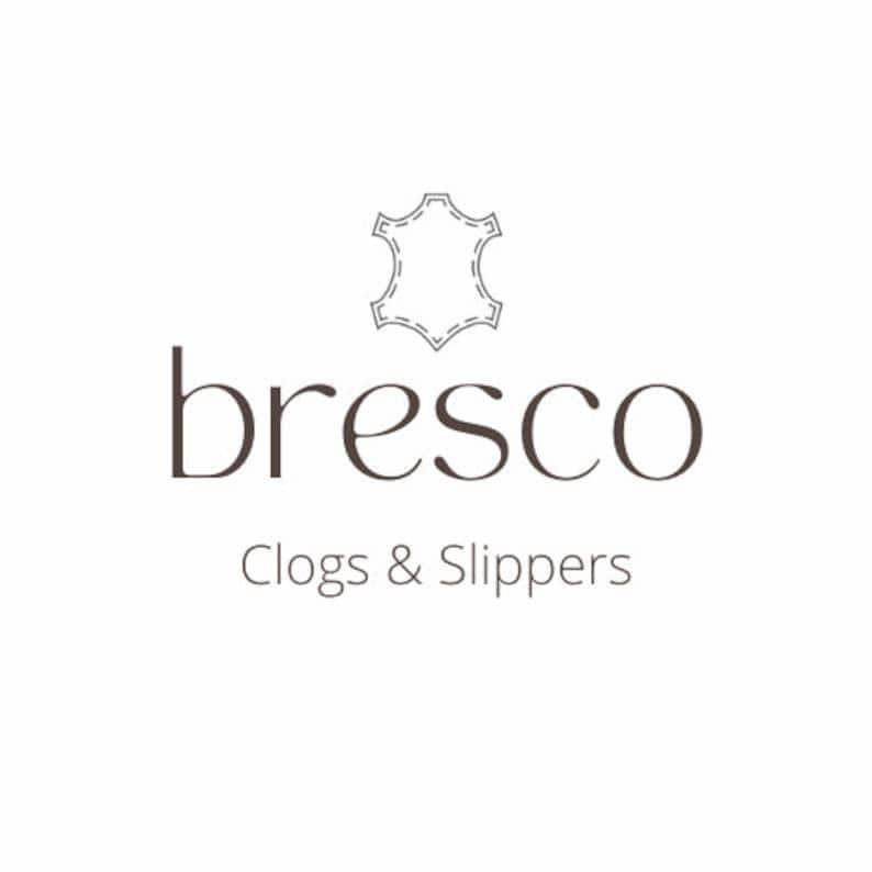May include: The logo for "bresco" features the brand name in a dark brown serif font, with the words "Clogs & Slippers" below. Above the name is a stitched leather icon, all set against a white background.
