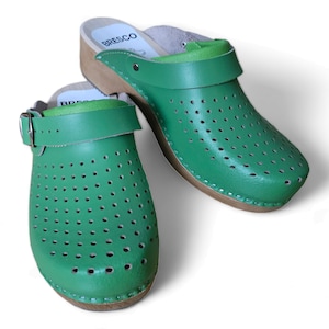 May include: A pair of green leather clogs with a wooden sole and a buckle strap. The clogs have a perforated design.