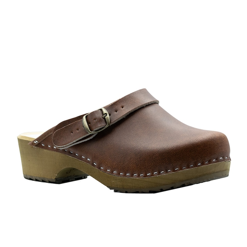 Classic Swedish wooden clogs made of natural cowhide leather in antic brown color and light wooden bottom with orthopedic profile. The upper has a strap with a buckle to adjust the length of the fastening on the heel. Available in women and men size