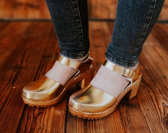 Heeled wooden clogs of natural leather with closed toe uppers on high heel with strap and buckle on heel in gold or pink color from Bresco