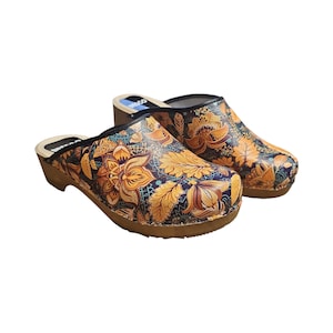 Puede incluir: Un par de zuecos de madera con estampado floral. Los zuecos son negros con un estampado floral amarillo, naranja y azul.