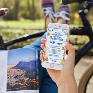 May include: A smartphone displaying a digital invitation for a birthday breakfast. The invitation is blue and white with a Bavarian theme and includes the text "Martin's Bavarian Birthday Breakfast" and "17.11. - 10:00".
