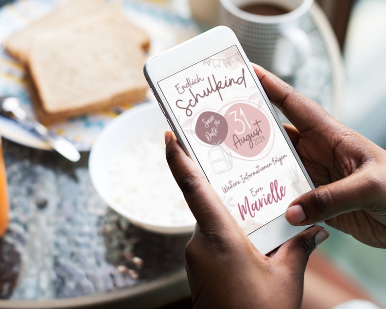 May include: A smartphone displaying a save the date announcement for a school-aged child's birthday party. The announcement is pink and white with the text "Endlich Schulkind" and "Save the Date" with a date of August 31, 2023. The announcement also includes the text "Weitere Informationen folgen" and "Eure  Marielle".