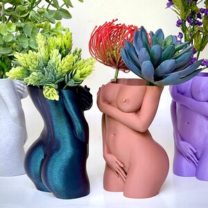 K&ouml;nnte beinhalten: Vier dekorative Vasen in Form des menschlichen K&ouml;rpers, jede mit einer anderen Farbe und einer anderen Pflanze darin. Die Vasen sind aus einem glatten, gl&auml;nzenden Material gefertigt und haben ein realistisches Aussehen. Die Pflanzen sind in verschiedenen Gr&uuml;nt&ouml;nen und Blau.