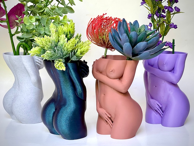 K&ouml;nnte beinhalten: Vier dekorative Vasen in Form des menschlichen K&ouml;rpers, jede mit einer anderen Farbe und einer anderen Pflanze darin. Die Vasen sind aus einem glatten, gl&auml;nzenden Material gefertigt und haben ein realistisches Aussehen. Die Pflanzen sind in verschiedenen Gr&uuml;nt&ouml;nen und Blau.