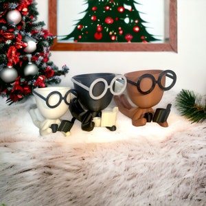 May include: Three ceramic planters shaped like people wearing glasses and reading books. The planters are black, white, and brown.