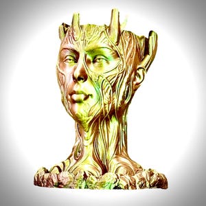 May include: A gold-coloured sculpture of a human head with a tree-like texture. The sculpture is detailed with intricate patterns and has a base that resembles roots.