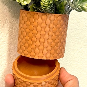 May include: A brown, textured, cylindrical planter with a removable top. The planter is made of a plastic-like material and has a wavy pattern.