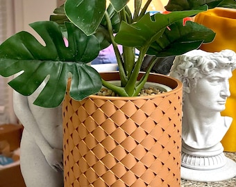 May include: A potted plant with large green leaves in a brown textured ceramic planter. The planter has a diamond pattern.