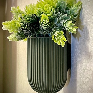 Peut inclure: Un pot en céramique côtelé vert foncé avec une petite composition de plantes vertes feuillues.
