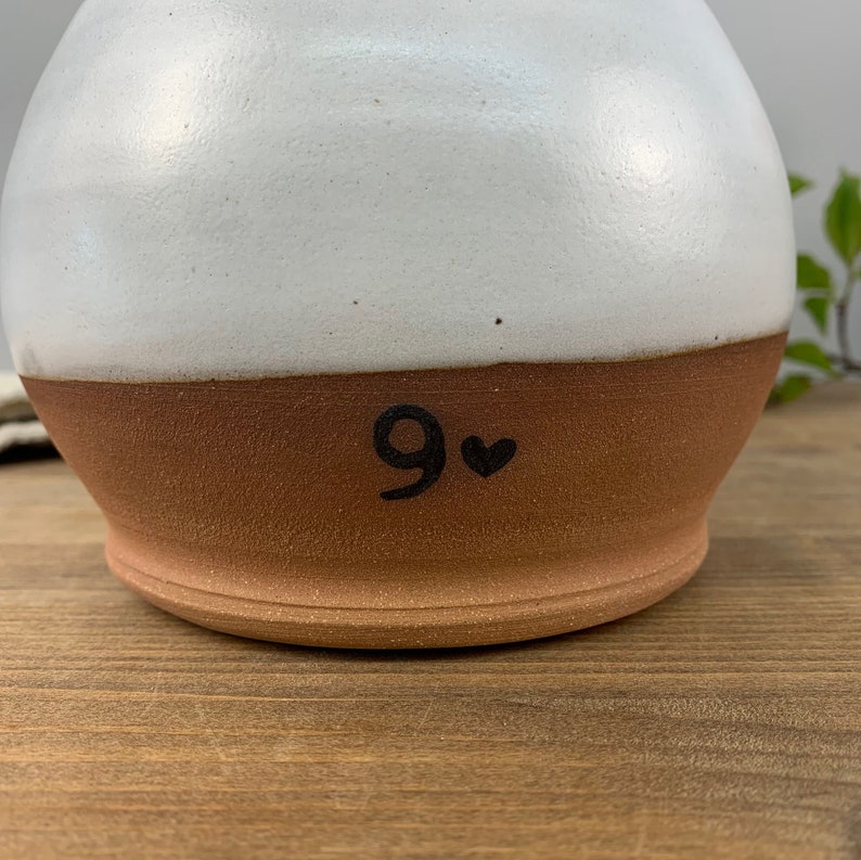 May include: White and brown ceramic pitcher with a black number 9 and a heart on the bottom.