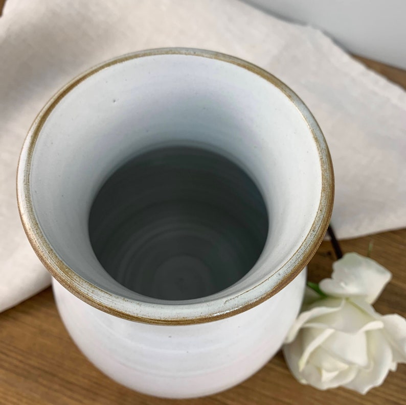 May include: White ceramic vase with a brown rim. The vase is empty and has a slightly rounded shape.