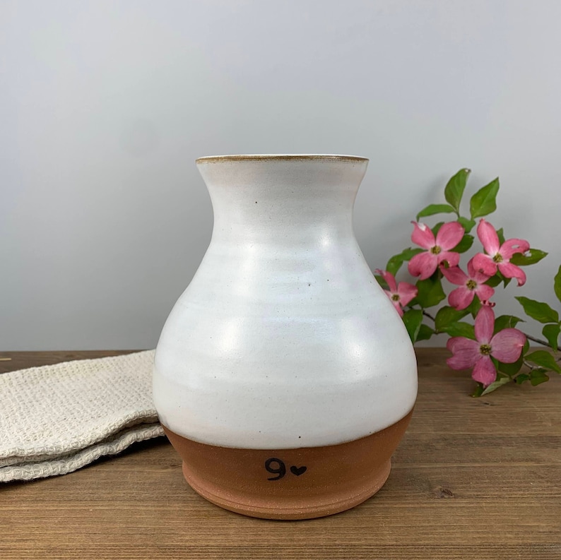 May include: White ceramic vase with a brown rim and base. The base has the number "9" and a heart drawn on it.