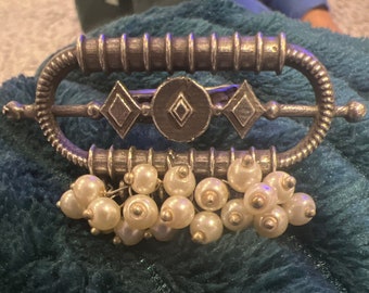 May include: A silver and gold brooch with a geometric design and a fringe of white pearls.