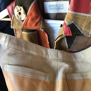 以下が含まれることがあります： パッチワークのデザインが施された茶色のコーデュロイジャケット。ジャケットは赤い革の襟と、「Patrick Cox Wannabe」という文字が書かれた白いラベルが付いています。