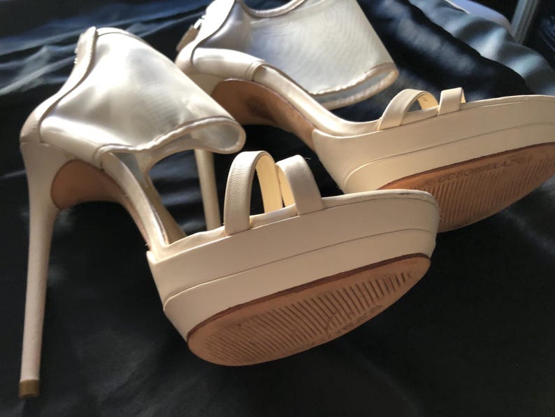 Puede incluir: Zapatos de tac&oacute;n alto con plataforma de color marfil con tacones de aguja. Los zapatos tienen m&uacute;ltiples correas y un detalle de malla en la parte superior. Las suelas son marrones. Los zapatos est&aacute;n sobre un fondo oscuro.