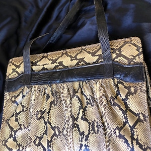 Op de afbeelding: Een vintage handtas gemaakt van slangenleer met een zwarte leren afwerking en twee zwarte leren banden. De tas heeft een geplisseerd ontwerp en een slangenleerpatroon.
