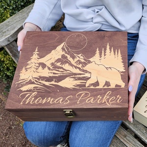 May include: Two wooden boxes with engraved mountain scenes and bears. The boxes are personalized with the name "Thomas Parker".
