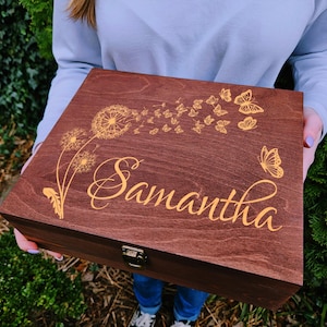 May include: A rectangular dark brown wooden keepsake box featuring a gold-colored engraved design on the lid. The design includes a dandelion with seeds transforming into a cluster of butterflies and the name Samantha in a cursive script font.