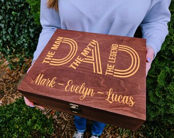 May include: A wooden box with a brown stain and gold lettering. The box says "DAD The Man The Myth The Legend" and has the names "Mark - Evelyn - Lucas" written below.