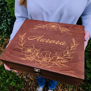 May include: A dark brown wooden box with a gold floral design and the name "Aurora" engraved on the lid.
