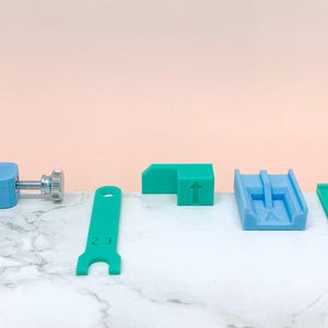 May include: A set of five tools for working with 3D printed objects. The tools are made of blue and green plastic and include a wrench, a clamp, a guide, and two spacers.