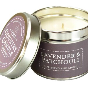 Puede incluir: Una vela en una lata plateada con una etiqueta morada que dice "The Country Candle Company" y "Lavender & Patchouli Uplifting and Light".