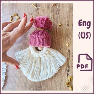 May include: A pink and white yarn gnome ornament with a wooden bead nose and a pink pom-pom hat. The ornament is hanging from a gold string. Eng (US) PDF