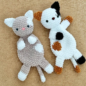 Può includere: Due peluche a forma di gatto realizzati a mano all'uncinetto con filato spesso e morbido. Un gatto è grigio chiaro e bianco con il naso rosa, l'altro è bianco con macchie nere e arancioni, occhi scuri e naso marrone. Entrambi hanno zampe bianche.