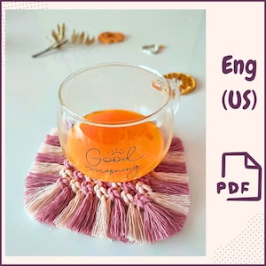 以下が含まれることがあります： オレンジジュースが入ったガラス製のマグカップが、ピンクと白のフリンジ付きのクロシェのコースターの上に置かれています。マグカップには「Good morning」と書かれています。