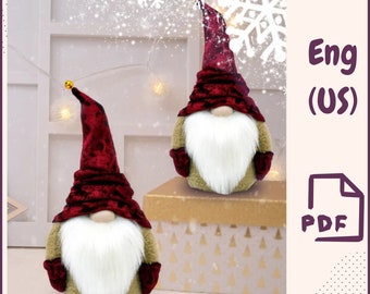 Può includere: Due gnomi di peluche con cappelli di velluto rosso e barbe di pelliccia bianca. Gli gnomi sono seduti su una scatola dorata e marrone con un motivo a fiocco di neve bianco.