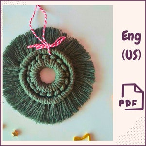 Könnte beinhalten: Handgefertigter Weihnachtsbaumschmuck aus Makramee in Olivgrün. Das kreisförmige Design hat eine gewebte Mitte und einen gefransten Außenrand. Zum Aufhängen wird eine rot-weiße Schnur verwendet. Das Bild enthält auch den Text "Eng (US)" und ein PDF-Symbol.